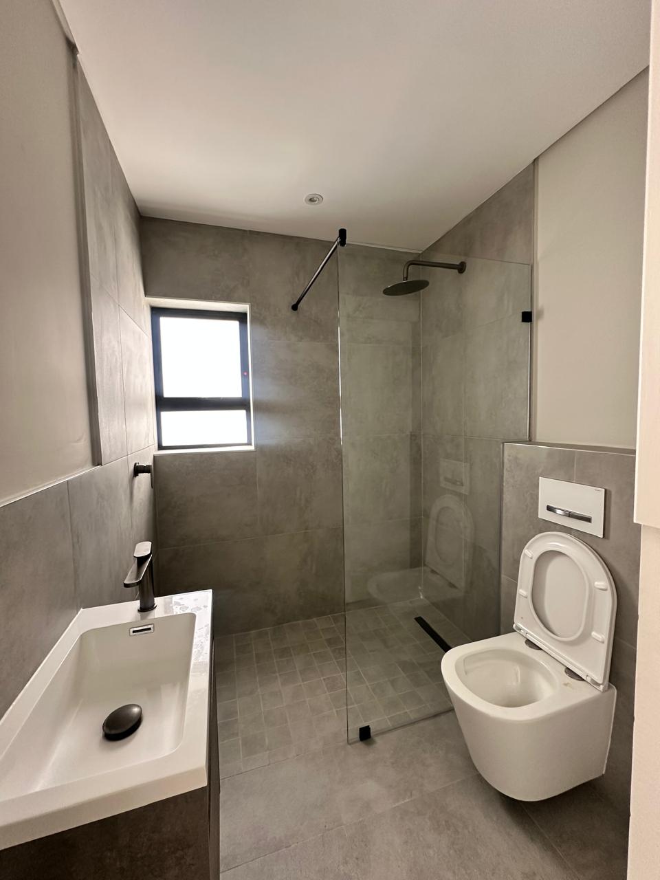 Completed bathroom — walk-in shower, wall-hung toilet and floating vanity in concrete-look tile