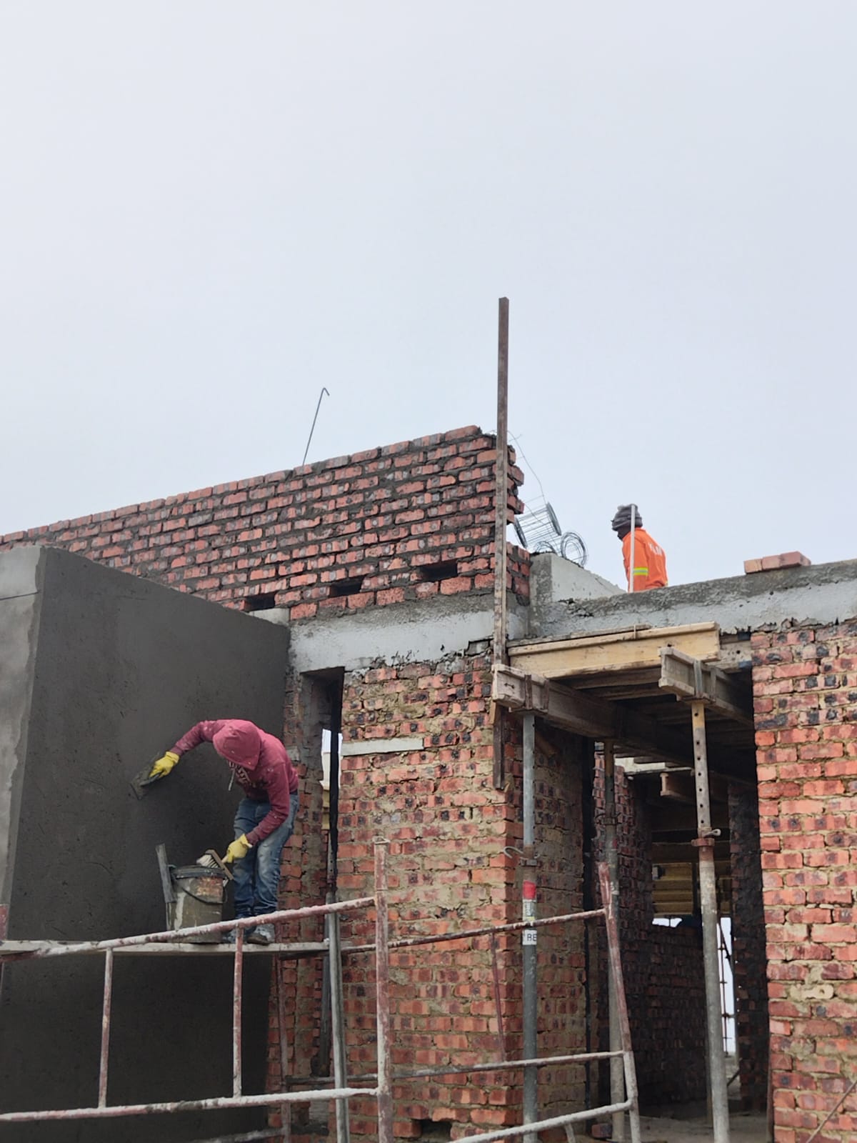Plasterer skimming a wall section as bricklayers continue overhead
