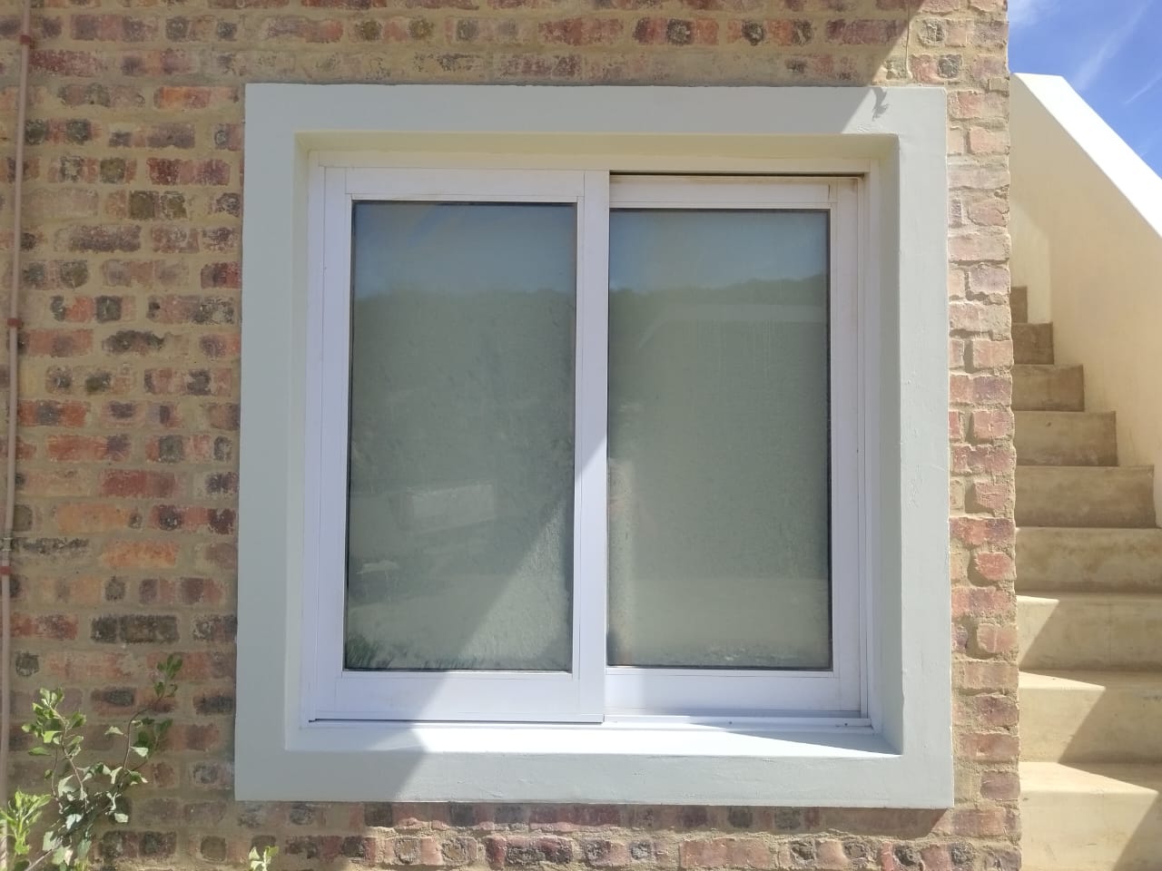 Newly installed aluminium sliding window with crisp plaster reveal on facebrick wall